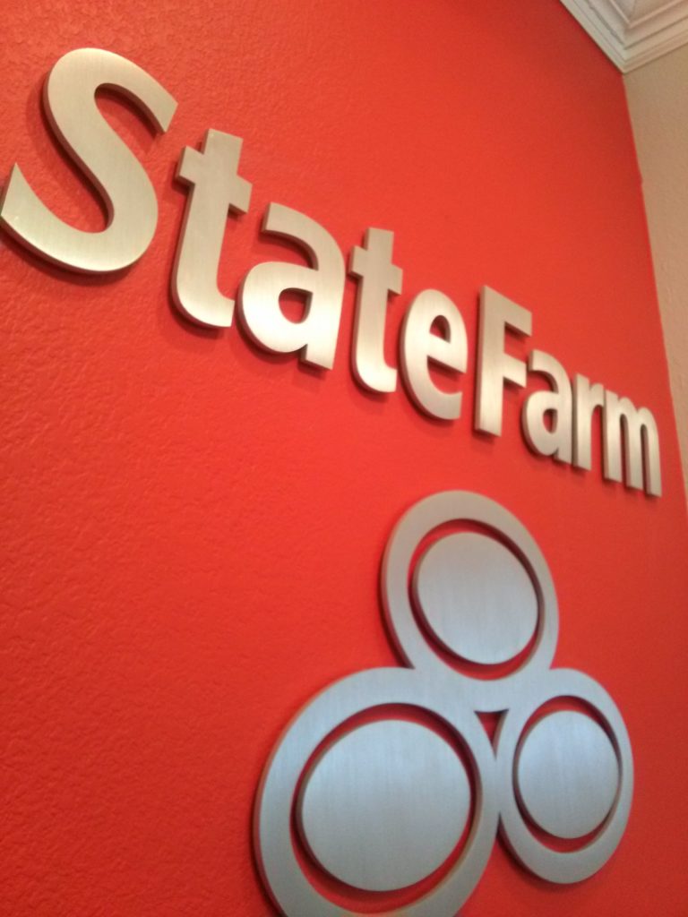State Farm interior wall sign with sliver letters on a red wall with the state farm logo underneath.